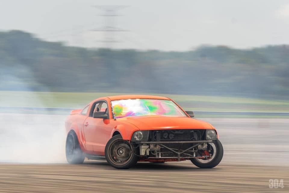 Orange Mustang mid-drift with tire smoke